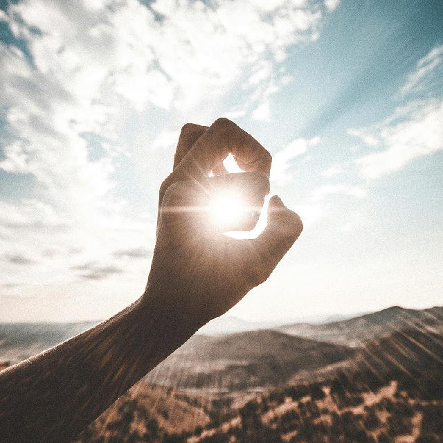 Hand framing sunlight over mountain landscape