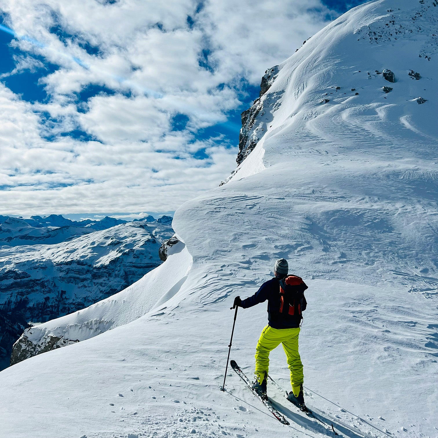 Skier on snowy mountain ridge under cloudy sky