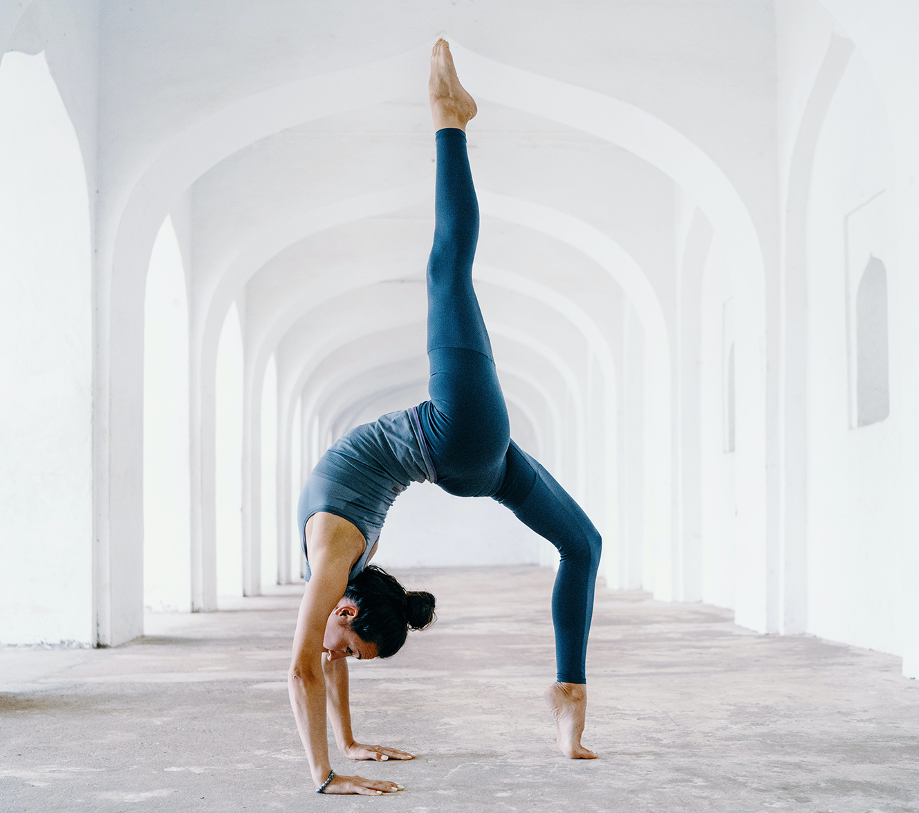 Woman doing yoga pose in white arched hallway